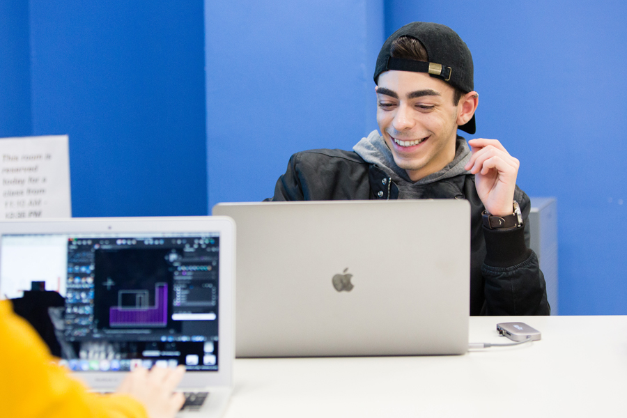 A student working on a laptop with another laptop screen visible in the foreground. 