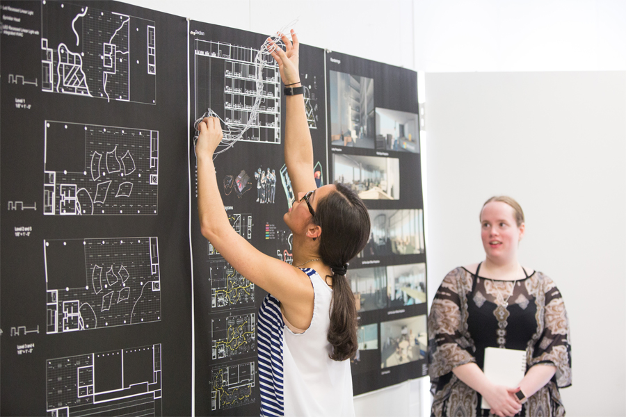 A student hands renderings on the wall for an interior design sketch.