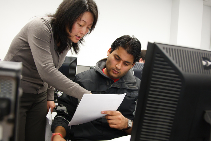 A faculty member interacting with a student in a computer lab. 