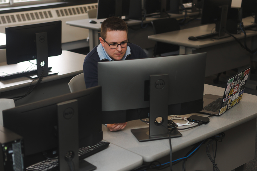 A student in a computer lab working a computer and a laptop.