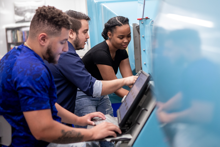 Three students are working on a piece of mechanical engineering equipment.