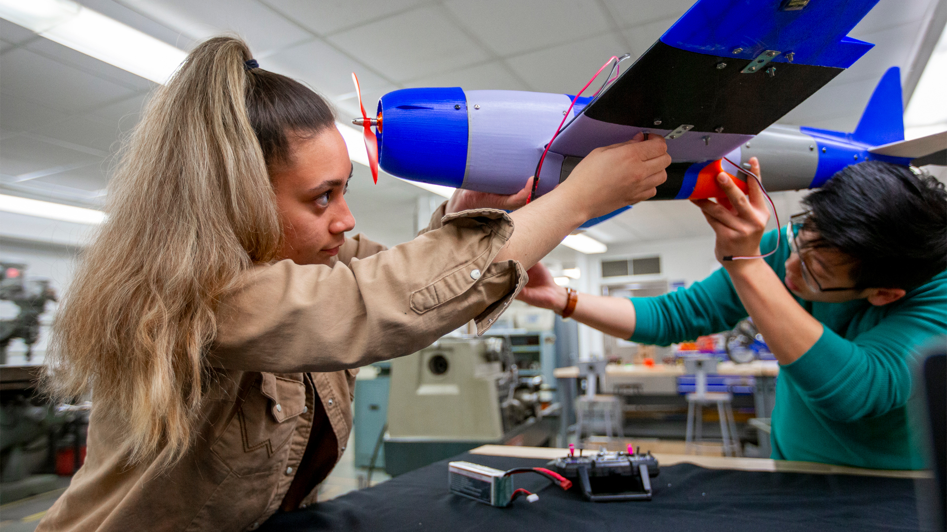 Two students in a lab working on a model airplane. 