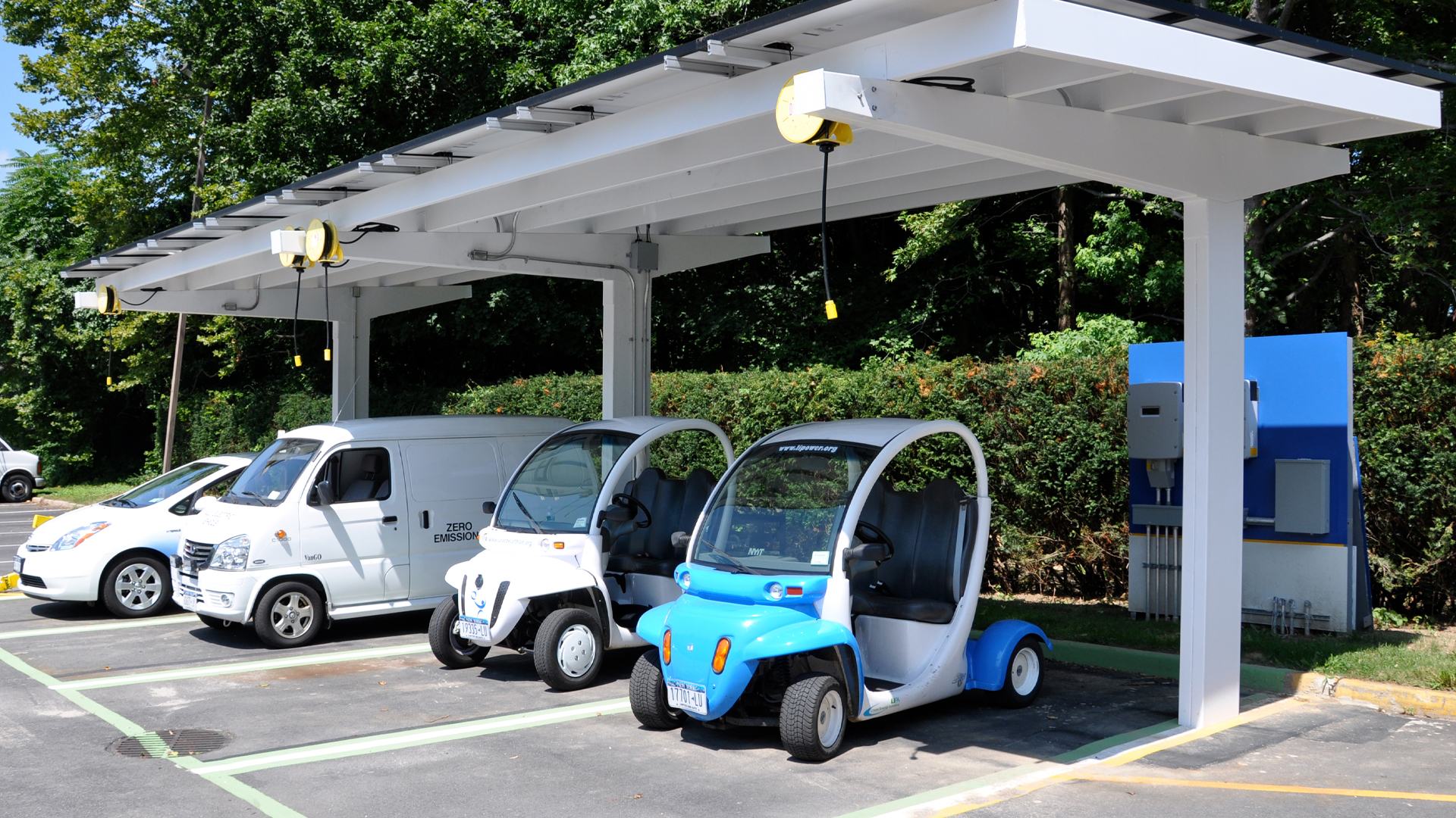 Several hybrid and electric vehicles parked under a solar charging station. 