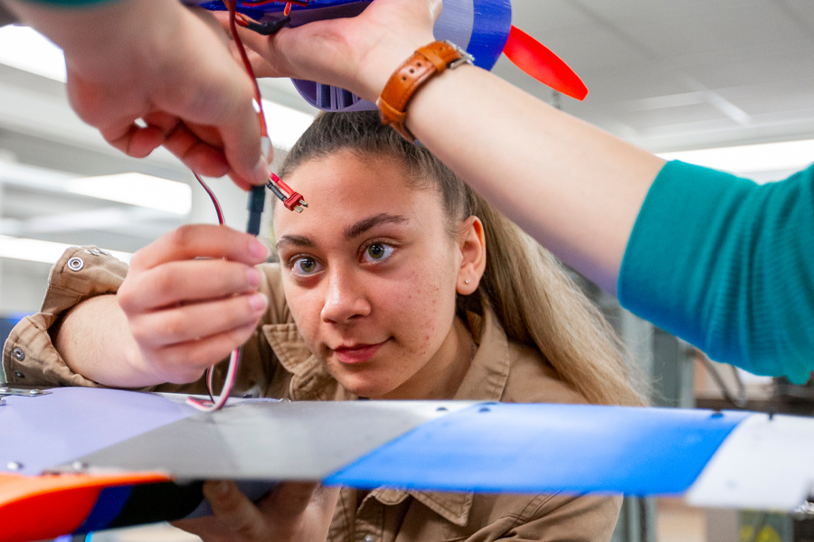 A female mechanical engineering student at New York Tech wires a model airplane with assistance from another student.