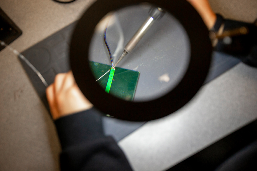 A close-up of a soldering iron being used on a circuit board through a magnifying glass. 