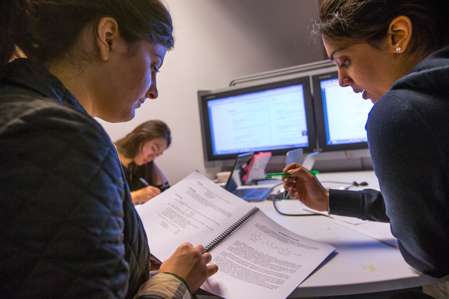 Two student review notes on a large table with two screens in the background.