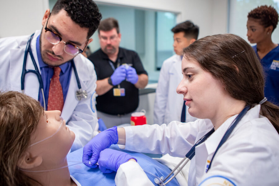 Two medical students work on a simulated patient in a clinical classroom.