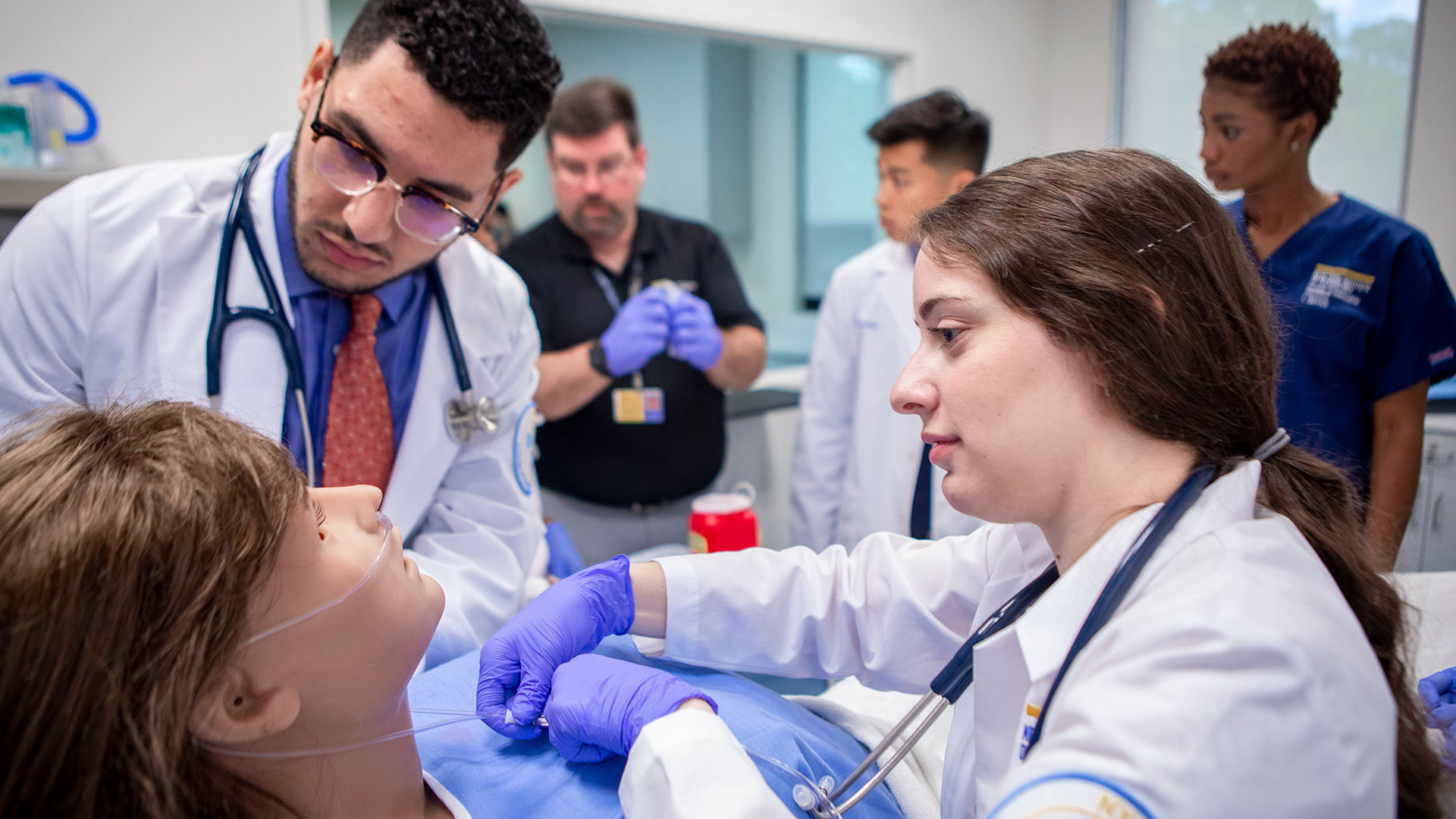 Two medical students work on a simulated patient in a clinical classroom.