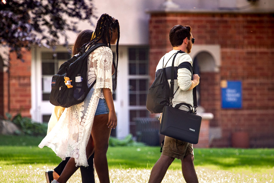 Three students with backpacks and laptop bags walk outdoors through New York Tech's campus.