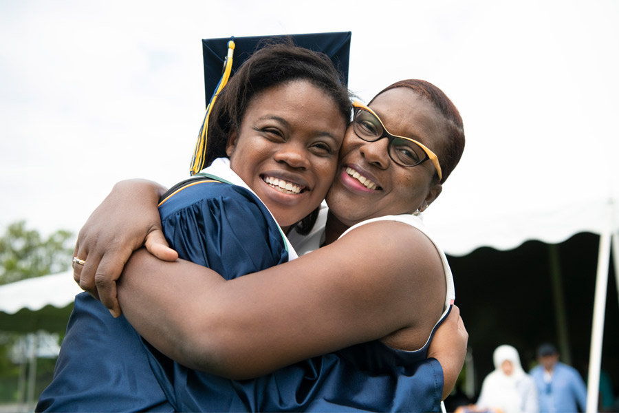 A parent hugs their New York Tech graduate wearing a graduation cap and gown during commencement.