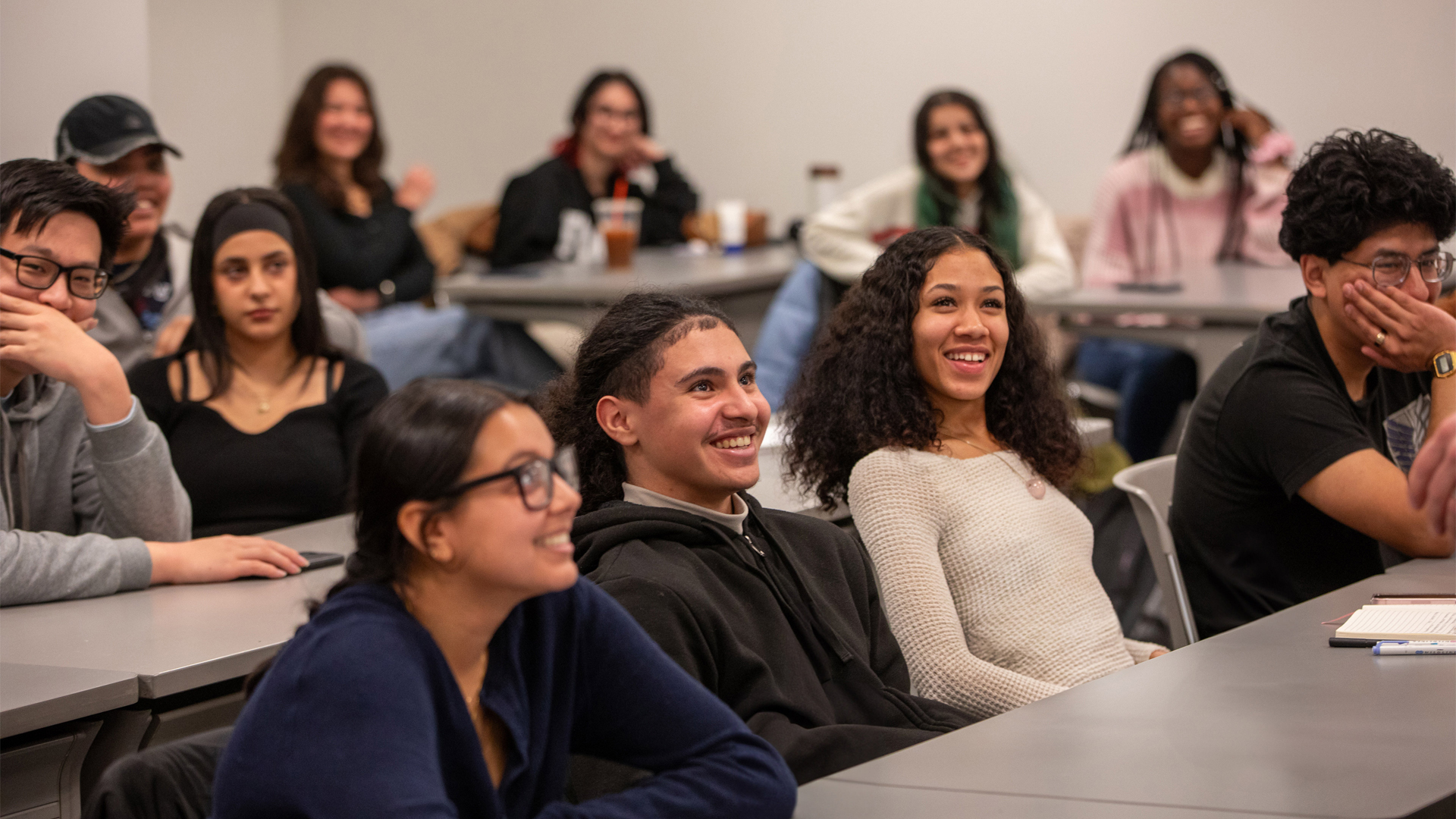 Student sitting at long tables in a lecture hall at New York Tech smile or laugh during a discussion related to financial aid.