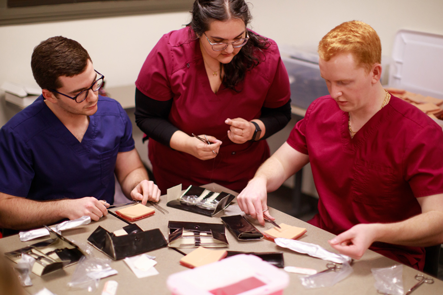 Student in scrubs preparing medical supplies around a table.