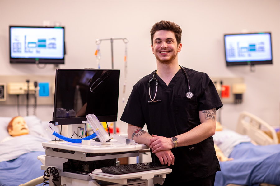 I student poses for a picture in a simulation lab with medical equipment.