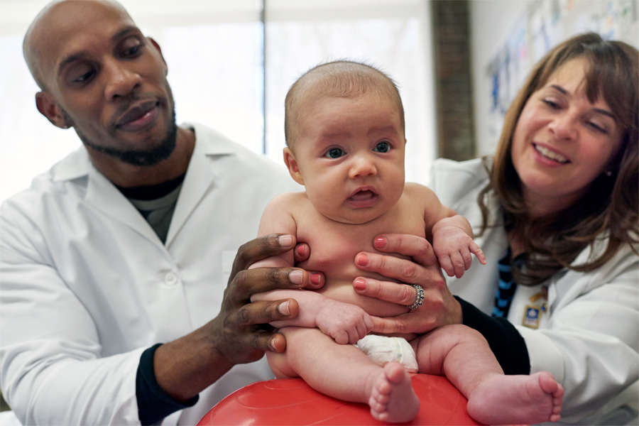 Two people in white coats hold a baby. 