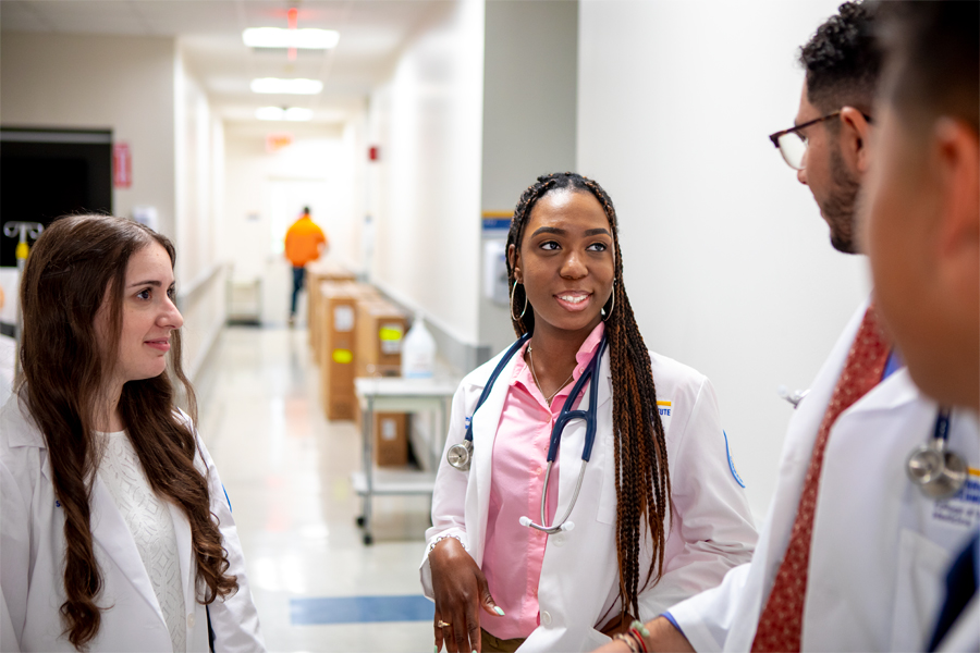 Three students in white coats and stethoscopes conversing