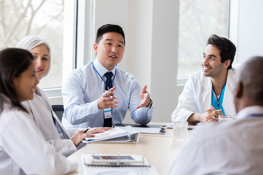 A group of people, some with white coats sitting in a conference room at a large table.