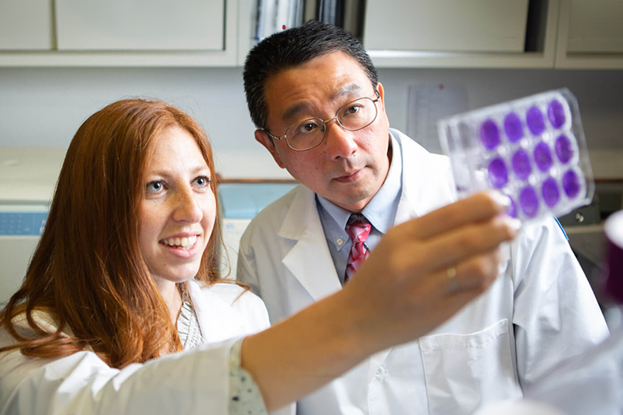 A student and professor hold up experimental items in the Center for Cancer Research.