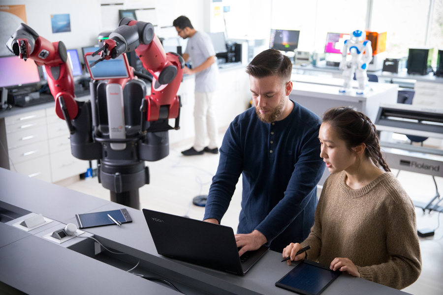 Two students are at a laptop programming a large, red robot in the Entrepreneurship and Technology Innovation Center.