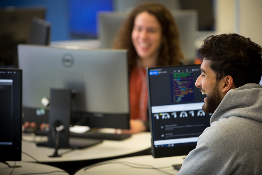 Two student sit across from each other in a computer lab.