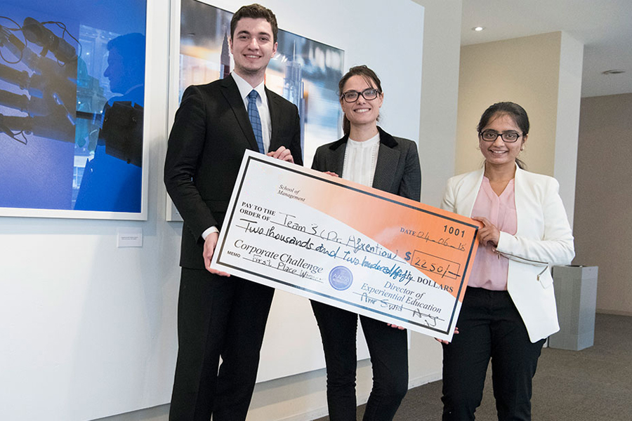 Three New York Tech School of Management students hold a large check after placing first in the Annual Fed Challenge.