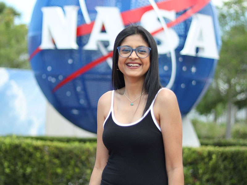 New York Tech School of Management student Bhavi Doshi stands outdoors in front of the NASA logo.