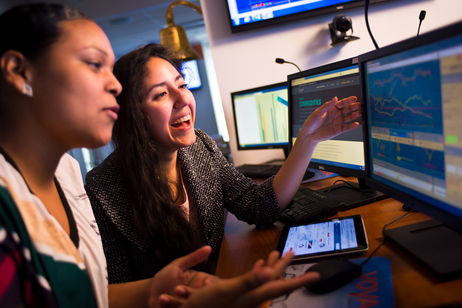 Two New York Tech School of Management students learn about stocks and entrepreneurship while using two computer screens and a tablet.