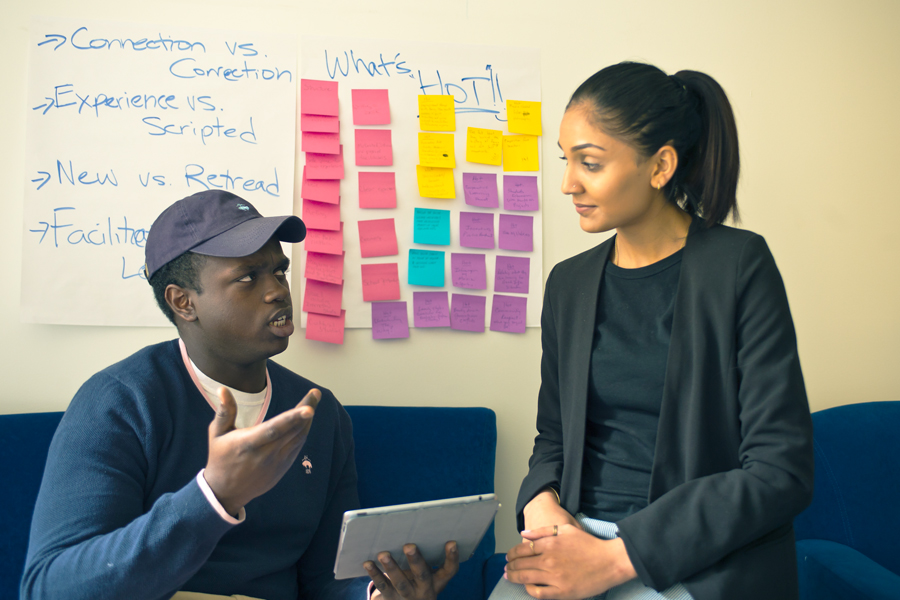 Two students discuss a project while using post-its on a large board to map out their plans.