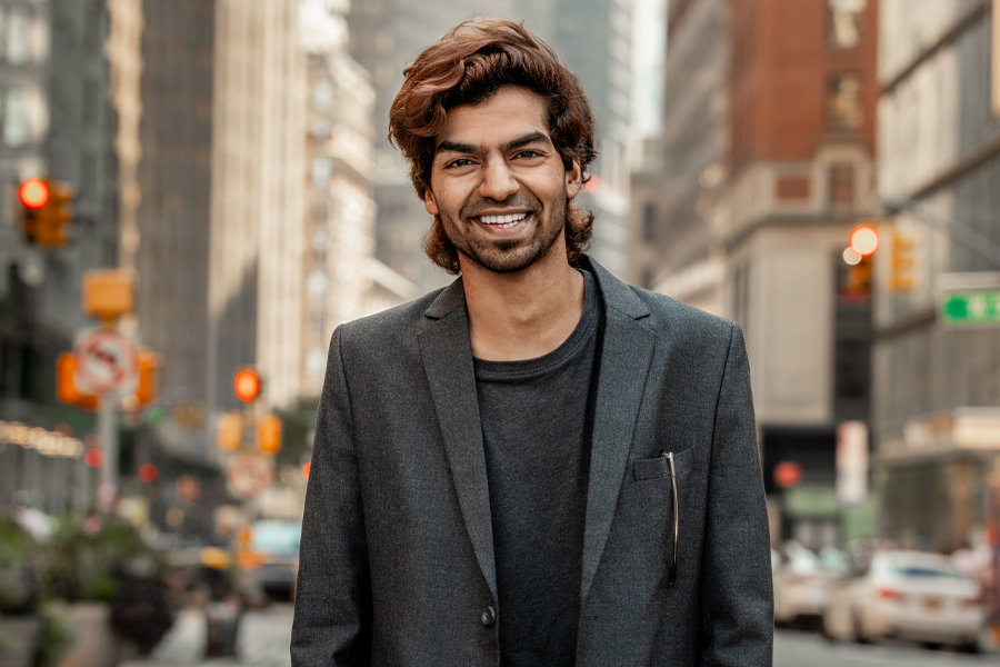 A New York Tech School of Management student wearing a blazer smiles while standing in a busy section of Manhattan.