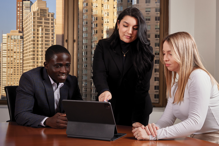 An employee from a partnering organization points to a tablet in a conference room while two New York Tech School of Management students observe.