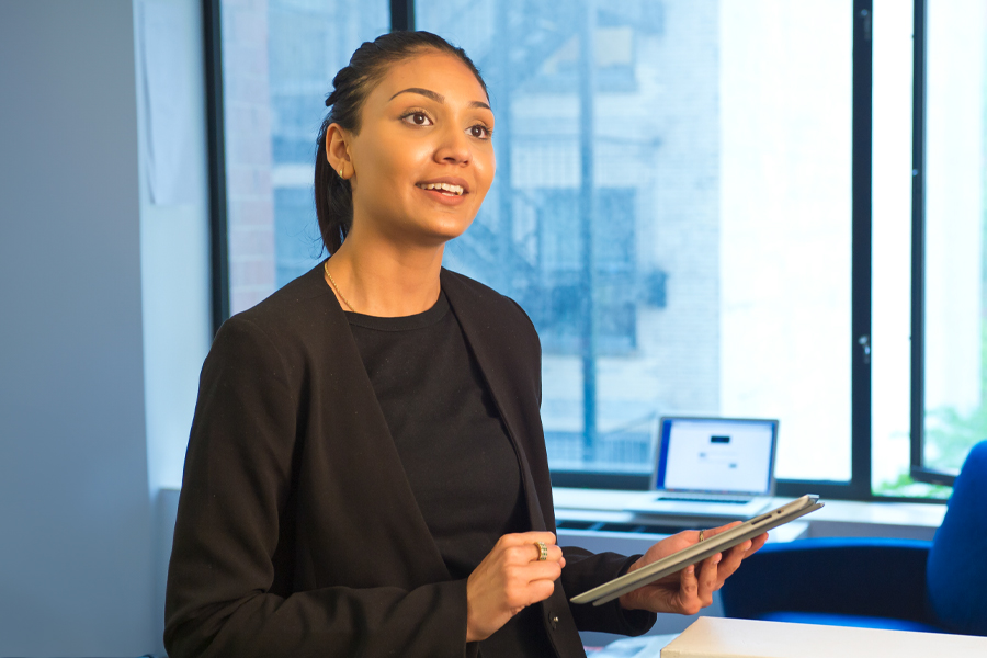 A person wearing business attire in a professional office holding a tablet. 