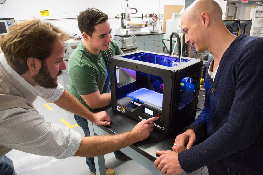 Three students working in a lab with a 3D printer.