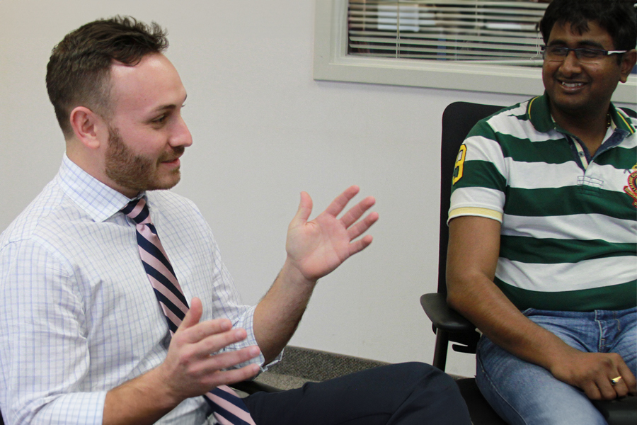 A person seated speaking with his hands up while other seated around him listen.