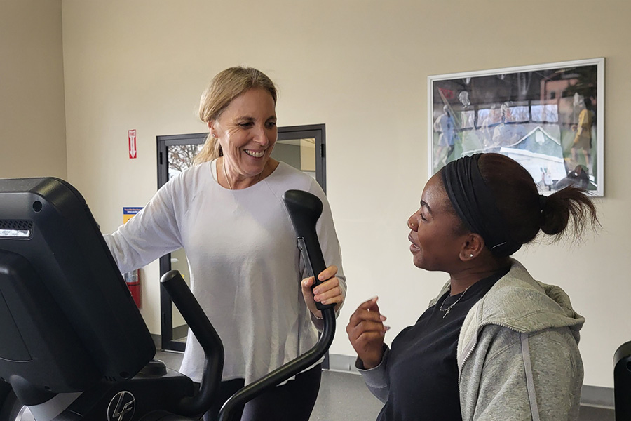 Woman standing next to woman on an elliptical