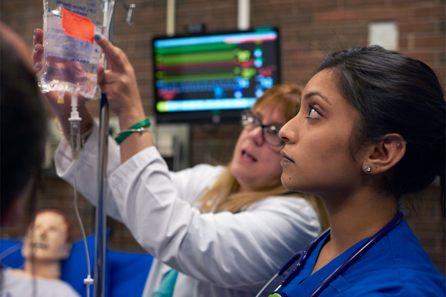 A nursing professor pointing to a label on an IV bag as a student looks on. 