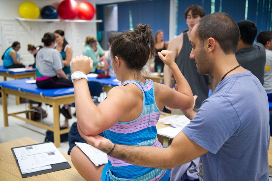 An occupational therapy student assisting someone to test range of motion on a medical examination table.