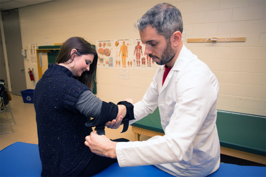 A person is applying a supportive elbow strap to a student.