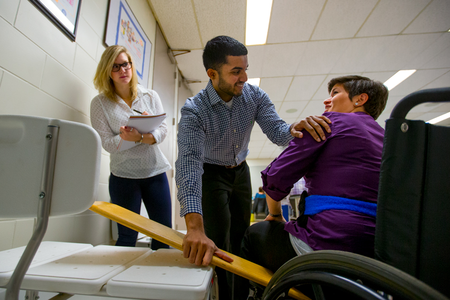 An occupational therapy student being observed interacting with a patient in a wheel chair.