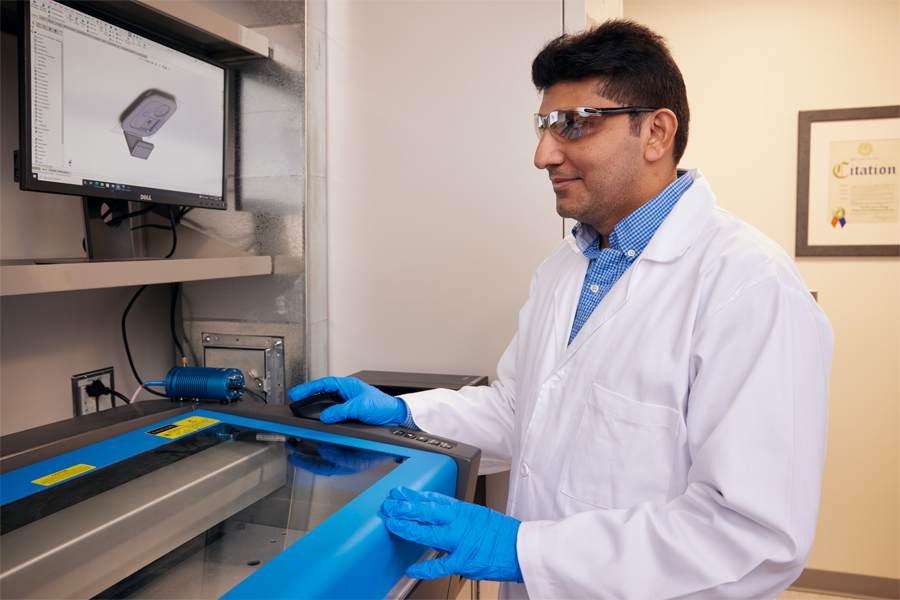 A faculty member wearing a white lab coat and protective gear conducting research in a lab. 