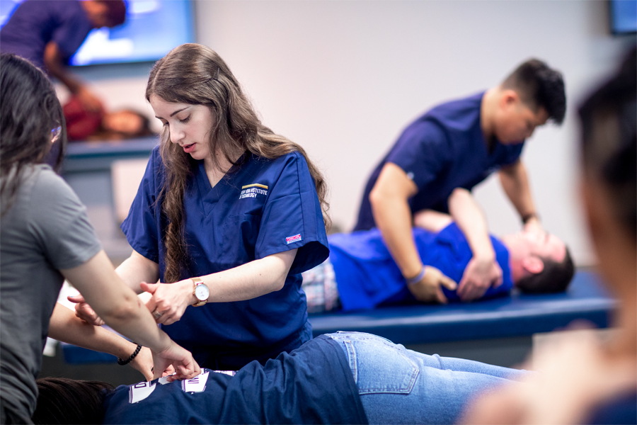 Students performing manipulations on a patient laying face down on an examination table.