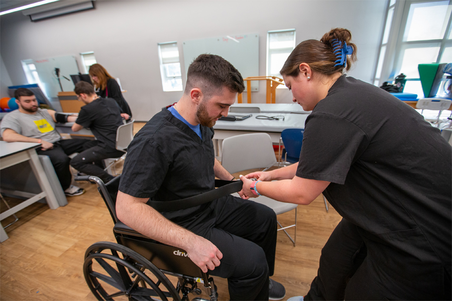 A physical therapy student helps a patient out of a wheelchair. 