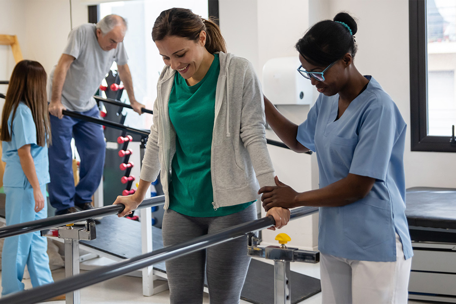 Two people undergoing physical therapy for walking assistance accompanied by physical therapists.