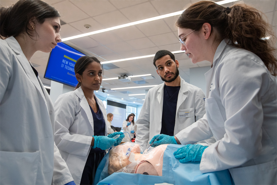 Four students in white coats practicing in a medical simulation lab.