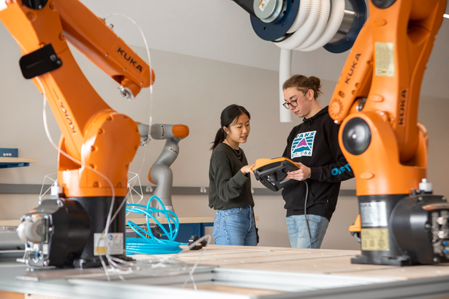 Two students in a lab for architecture behind two large mechanical arms.