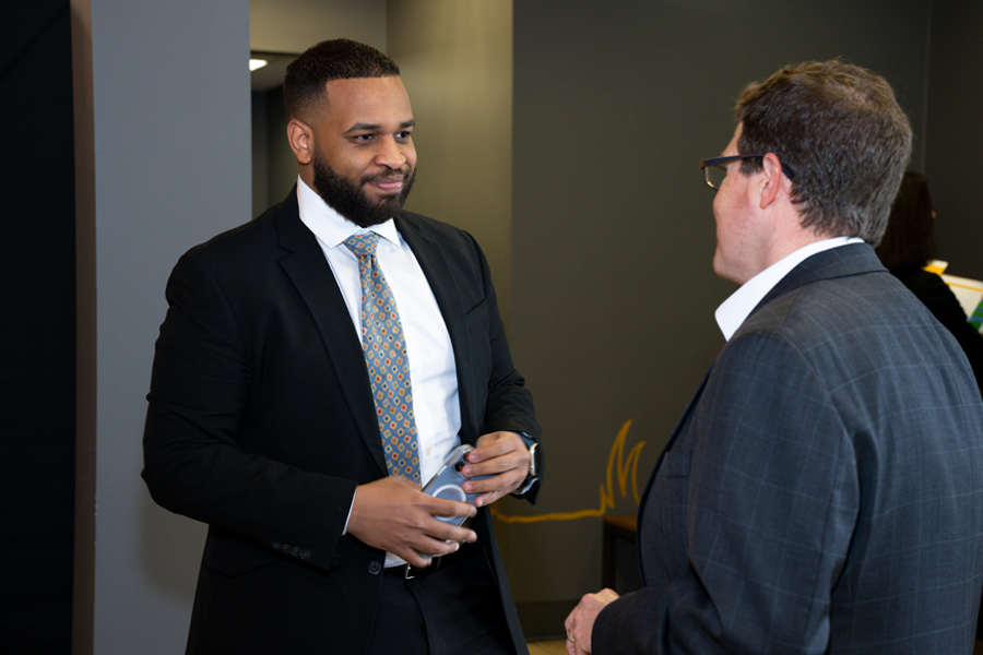 A man in a black suit talking with another man in a blue suit.