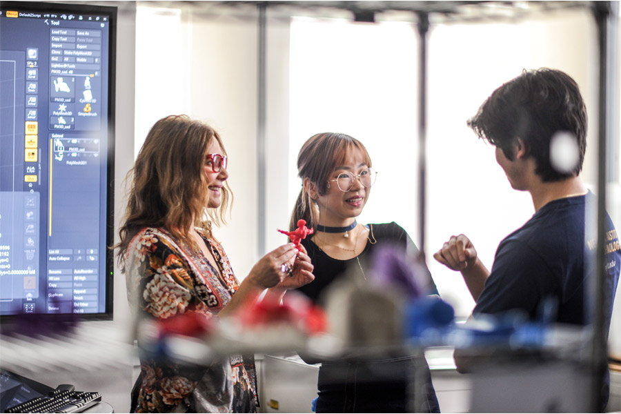 Three students in a lab. One of the is holding a 3D printed object. 