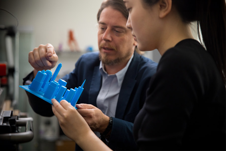 An instructor and a student holding a 3D printed model of buildings.